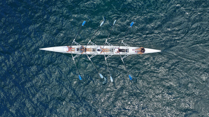Aerial drone bird's eye view of sport canoe operated by team of young trained athletes in deep blue Aegean sea