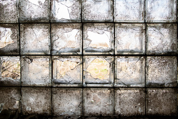 Partially broken, dirty window of glass blocks, on an abandoned farm, in the village. View from inside.