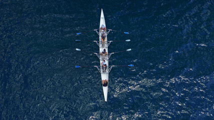 Aerial drone bird's eye view of sport canoe operated by team of young trained athletes in deep blue Aegean sea
