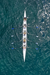 Aerial drone bird's eye view of sport canoe operated by team of young women in emerald open ocean...