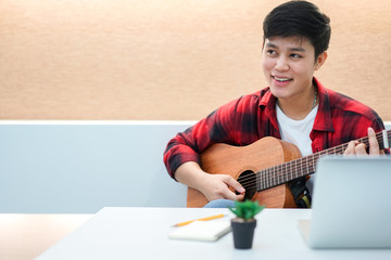 Close up young asian teenager boy open laptop for search song and playing classical guitar for practice or record live stream on social media , millennial lifestyle concept	