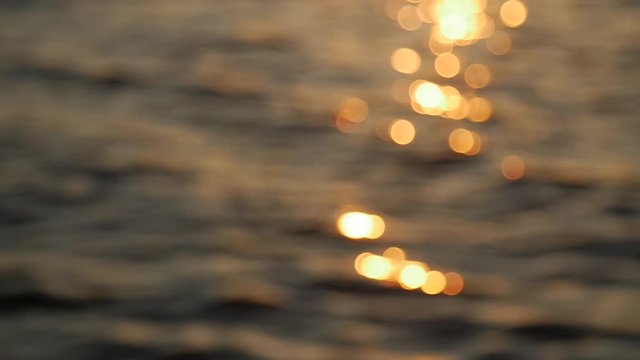 Beautiful golden colors of sunset, small waves with glossy reflexions. Out of focus, sunbeam reflection on calm water surface in evening, golden hour. Focus pulling from blur.