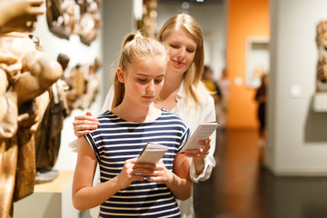 Woman with girl holding guidebook, standing in museum of ancient sculpture