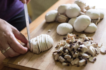 A woman cuts mushrooms with a knife on a wooden cutting board