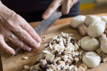 A woman cuts mushrooms with a knife on a wooden cutting board