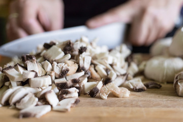 A woman cuts mushrooms with a knife on a wooden cutting board