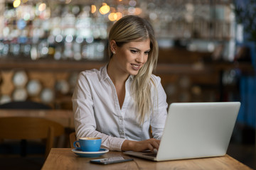 Young happy businesswoman typing an e-mail on laptop in a cafe