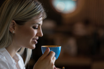 Close up of young happy woman enjoying in a cup of coffee  in a cafe.