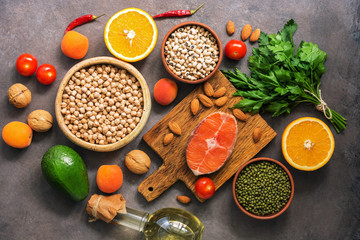 Concept healthy balanced food, salmon,legumes, fruits, vegetables, olive oil and nuts, dark rustic background. Flat lay, top view.