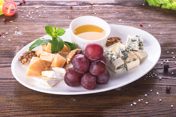 Fototapeta na wymiar Assorted cheeses with honey, walnuts and grapes on plate