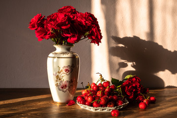 Fresh organic sweet cherries and bouquet of red roses in a white vase on wooden table
