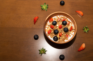 Fresh corn flakes cereal and fruits strawberry and blueberry in wood bowl