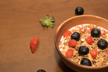 Fresh corn flakes cereal and fruits strawberry and blueberry in wood bowl
