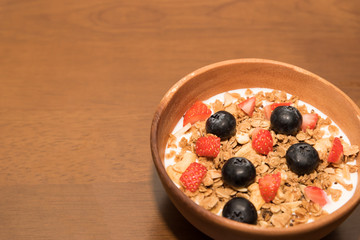 Fresh corn flakes cereal and fruits strawberry and blueberry in wood bowl