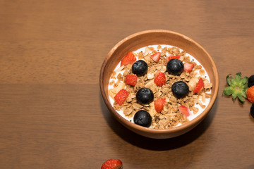 Fresh corn flakes cereal and fruits strawberry and blueberry in wood bowl