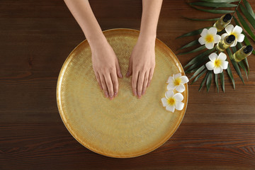 Fototapeta na wymiar Woman soaking her hands in bowl with water and flowers on wooden table, top view. Spa treatment
