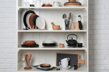 White shelving unit with set of dishware near brick wall
