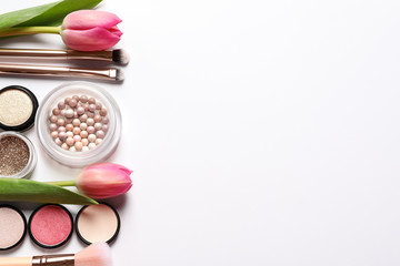 Different makeup products and flowers on white background, top view