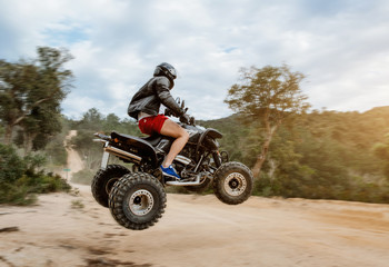 The quad racer is jumping on the dusty road. Quad bike off-road. Quad bike in action.