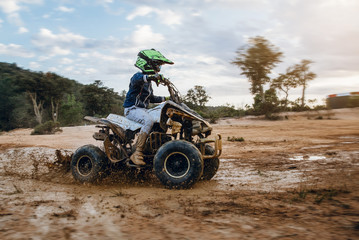 A child rides a quad bike through the mud. ATV rider rides on the dirt