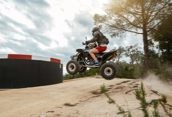 The quad racer is jumping on the dusty road. Quad bike off-road. Quad bike in action.