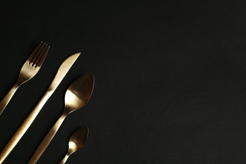 Set of gold cutlery on black background, flat lay. Space for text
