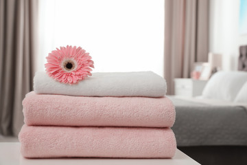 Stack of clean towels with flower on table in bedroom