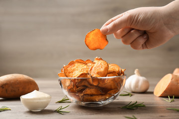 Woman taking sweet potato chip from bowl on table, closeup