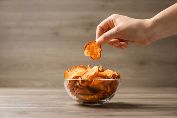 Woman taking sweet potato chip from bowl on table, closeup