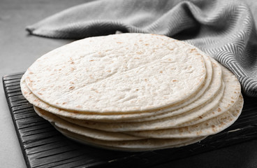 Wooden board with corn tortillas on table, closeup. Unleavened bread