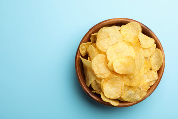 Delicious crispy potato chips in bowl on color background, top view with space for text