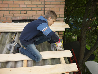 Teenager boy help to repair the roof of a home with hammer and drill