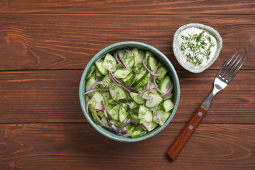 Flat lay composition with delicious fresh cucumber onion salad in bowl served on wooden table