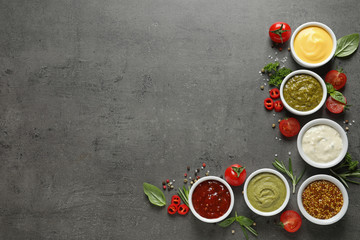 Bowls with different sauces and ingredients on gray background, flat lay. Space for text
