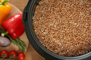 Delicious buckwheat in multi cooker and vegetables on wooden table, top view