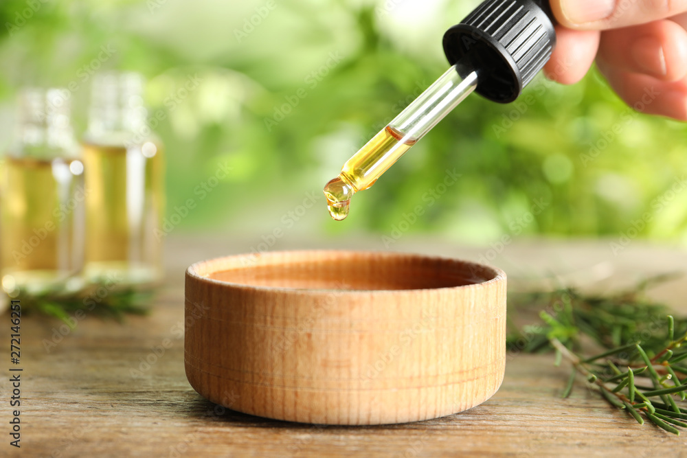 Wall mural woman dripping natural tea tree oil in bowl on table, closeup