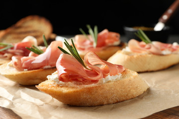 Tasty bruschettas with prosciutto and cream cheese served on table against dark background, closeup. Space for text