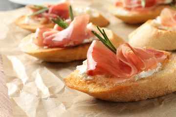 Tasty bruschettas with prosciutto and cream cheese on parchment, closeup. Space for text