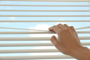 Woman opening horizontal window blinds at home, closeup. Space for text