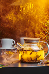 Ceylon tea in a transparent teapot on a smoky gray background with warm lighting and decorated with...