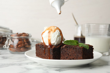 Plate with fresh brownies and ice-cream on table. Delicious chocolate pie