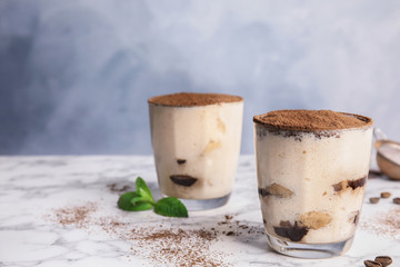 Two glasses of tiramisu cake on table against color background, space for text