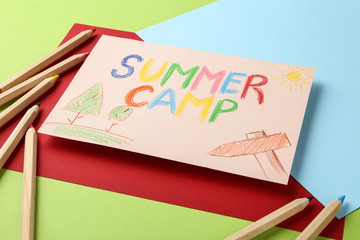 Paper with written text SUMMER CAMP, drawings and different pencils on color background, closeup