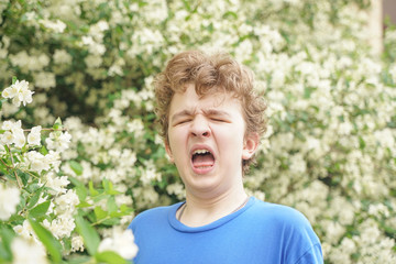 Naklejka na ściany i meble Teenager with allergies standing in a blue t-shirt among the Jasmine bushes and suffers from bad health