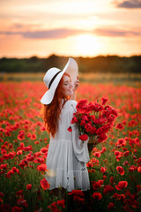 Happy Young beautiful female with bouquet of red poppies stands in flowered field at sunset