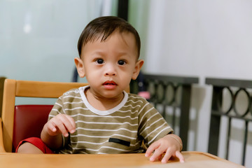 Portrait Of Happy Young Baby Boy In High Chair. Child sitting at empty table.Baby nutrition concept.Food advertisement design. smiling baby sitting on baby Chair.