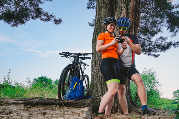 Fototapeta na wymiar Happy couple searching on map in smartphone destination. man and woman in helmets traveling mountain biking over rough terrain. Theme tourism and navigation, search way, create route, gps phone app