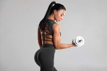 Fitness woman doing exercise for biceps on gray background. Muscular woman workout with dumbbells - obrazy, fototapety, plakaty