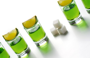 Absinthe green liquor in glasses. Alcoholic hallucinogenic beverage. White background. Pieces of...