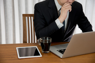 Businessman working at laptop with a cup of coffee. Businessman thinking and sitting on teak wood table.